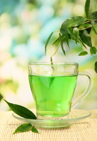 Прозрачный чашка зеленого чая на бамбуковом коврике, на фоне природы — стоковое фото