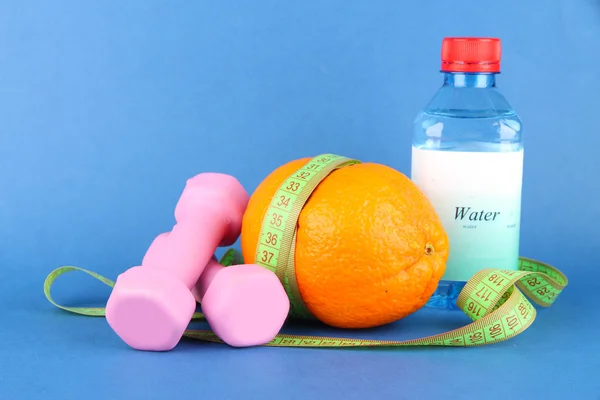 Oranje met het meten van tape, halters en fles water, op een achtergrond met kleur — Stockfoto