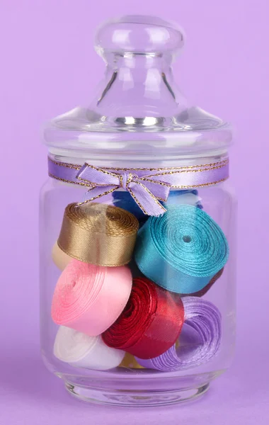Tarro de vidrio que contiene varias cintas de colores sobre fondo lila —  Fotos de Stock