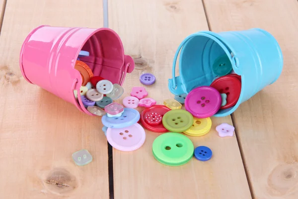 Colorful buttons strewn from buckets on wooden background — Stock Photo, Image