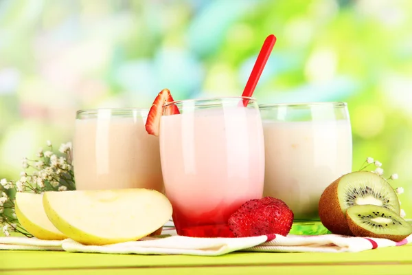 Delicious yogurts with fruits in glasses on wooden table on natural background — Stock Photo, Image