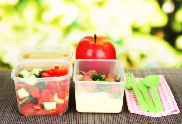 Tasty lunch in plastic containers, on bamboo mat on bright background — Stock Photo, Image