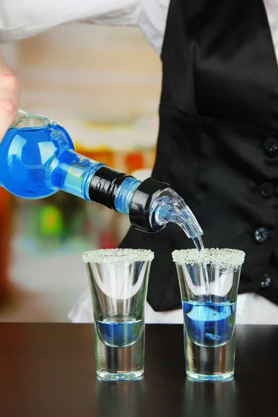 Barmen hand with bottle pouring beverage into glasses, on bright background — Stock Photo, Image