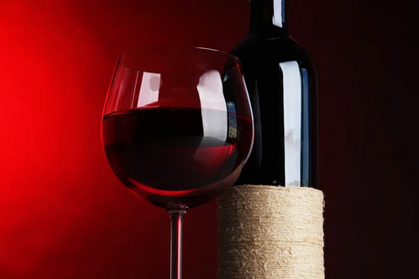 Glass of wine with bottle on bright red background — Stock Photo, Image