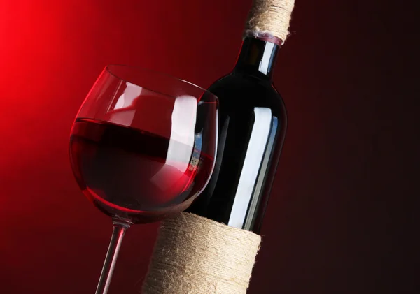 Bicchiere di vino con bottiglia su sfondo rosso brillante — Foto Stock