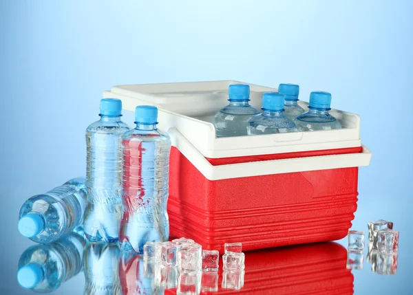 Refrigerador viajero con botellas de agua y cubitos de hielo, sobre fondo azul —  Fotos de Stock