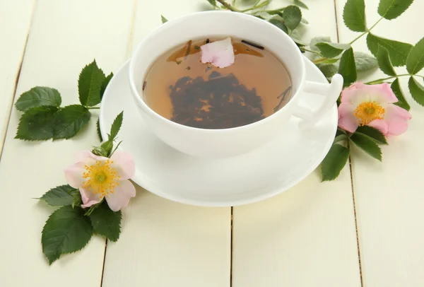 Tazza di tisana con fiori di rosa mosqueta sul tavolo di legno bianco — Foto Stock