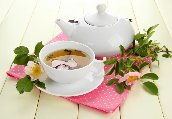 Κύπελλο και teapot τσαγιού από βότανα με ισχίου ροδαλά λουλούδια στο λευκό ξύλινο τραπέζι — Φωτογραφία Αρχείου