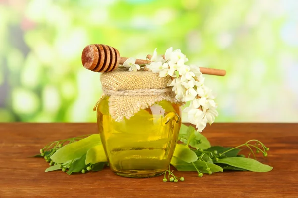 Sklenice medu s květy, vápna, akátu na dřevěný stůl na světlé pozadí — Stock fotografie