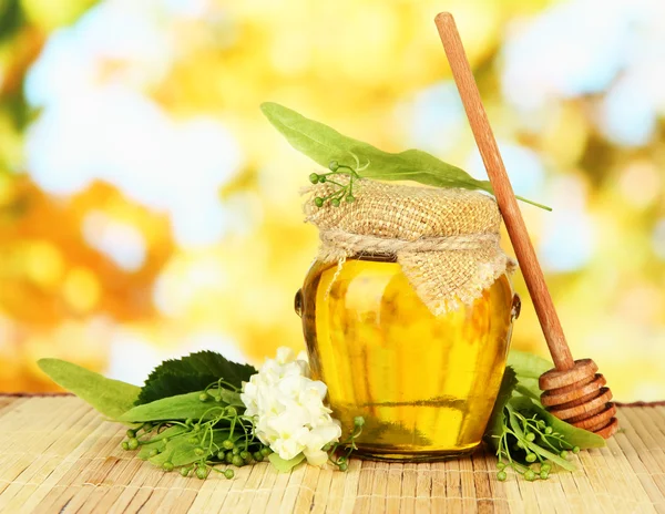 Glas Honig mit Blüten aus Kalk, Akazie auf farbiger Bambusmatte auf hellem Hintergrund — Stockfoto