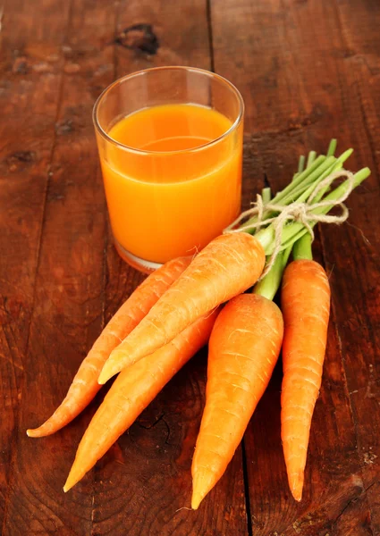 Karottenhaufen, Glas Saft, auf Holzgrund — Stockfoto