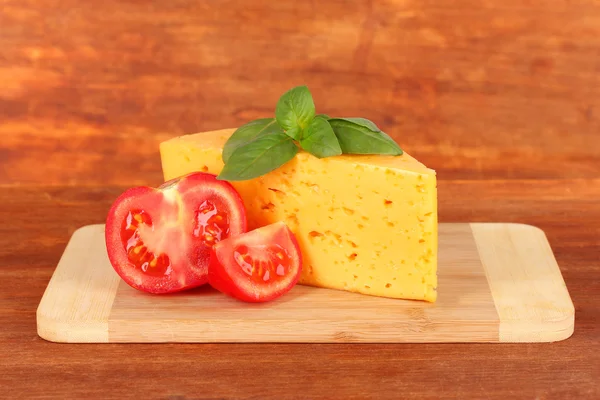 Sýrem, bazalkou a rajčaty na prkénko na dřevěné pozadí — Stock fotografie