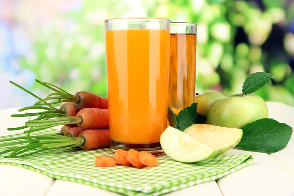 Glasses of juice, apples and carrots on white wooden table, on green background — Stock Photo, Image