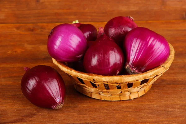 Lila Zwiebel im Weidenkorb auf hölzernem Hintergrund — Stockfoto