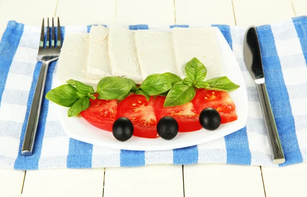 Sheep milk cheese, with basil and tomato on color napkin on wooden background — Stock Photo, Image