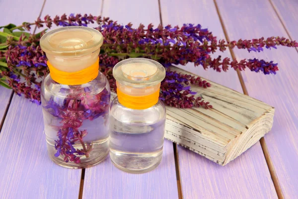 Geneeskundeflessen met salvia bloemen op paarse houten achtergrond — Stockfoto