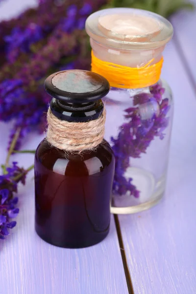 Medycyna butelek i szałwia kwiaty na fioletowym tle drewniane — Zdjęcie stockowe