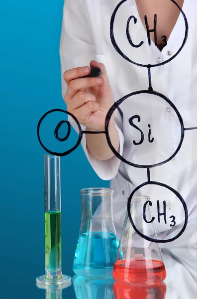 化学家女人在蓝色背景上的玻璃上写公式 — 图库照片