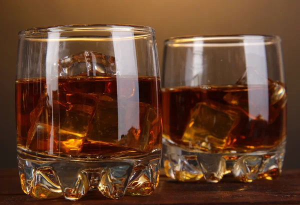 Copas de brandy con hielo sobre mesa de madera sobre fondo marrón — Foto de Stock