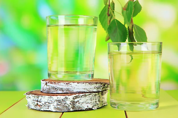 Glasses of birch sap on wooden table, on green background — Stock Image Glasses of birch sap on wooden table, on green background Stock Photo