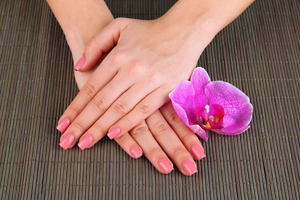 Nő kezet rózsaszín manikűr és orchidea, bambusz mat háttér — Stock Fotó