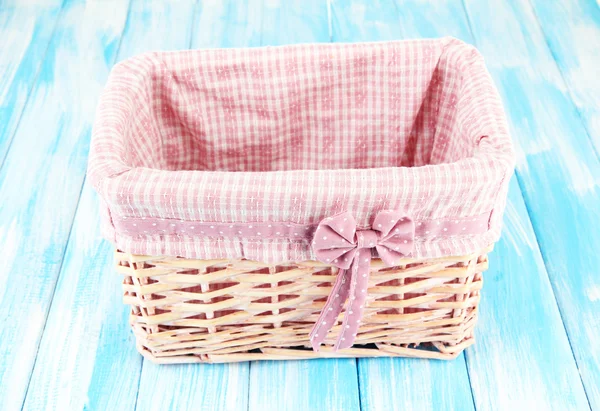 Wicket basket with pink fabric and bow, on color wooden background — Stock Photo, Image