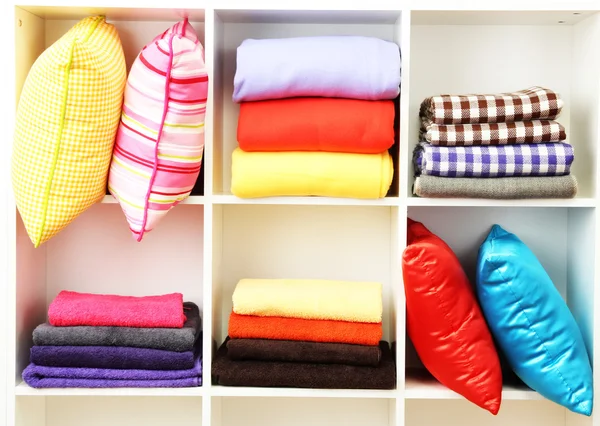 Bright pillows, towels and plaids on shelves, isolated on white — Stock Photo, Image