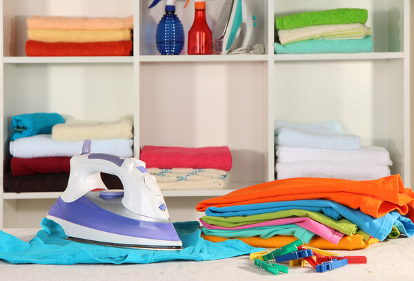 Одежда и утюг на столе на полках
