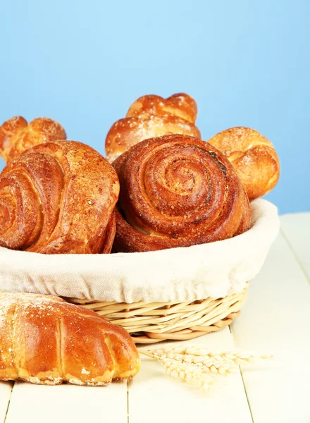 Composition with buns in wicker basket, on wooden table, on color background — Stock Photo, Image