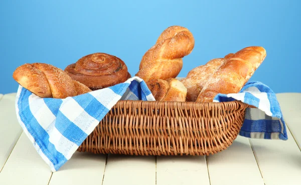 Composition with buns in wicker basket, on wooden table, on color background — Stock Photo, Image