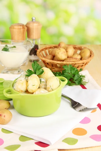 Anbudsförfarande unga potatis med gräddfil och örter i stekpanna på träbord på naturliga bakgrund — Stockfoto