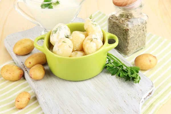 Las patatas tiernas jóvenes con la crema agria y las hierbas en la cacerola sobre el tablero de madera a la mesa el primer plano —  Fotos de Stock