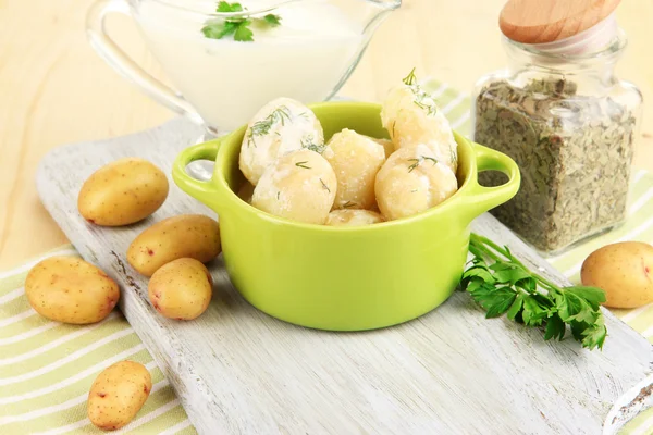 Batatas jovens macias com nata azeda e ervas na panela na tábua de madeira na mesa close-up — Fotografia de Stock