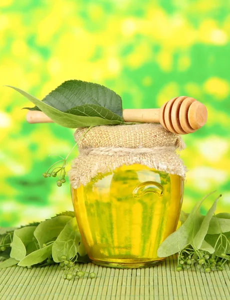 Jar of honey with flowers of lime, on color bamboo mat on bright background — Stock Photo, Image