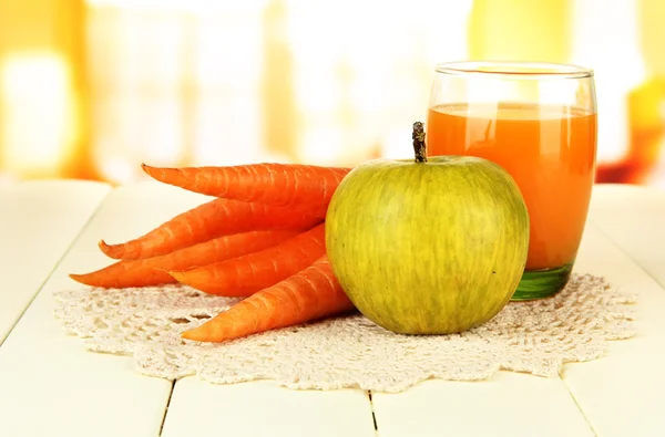 Heap de cenouras e maçã verde, vidro de suco, na mesa de madeira a cores no fundo brilhante — Fotografia de Stock