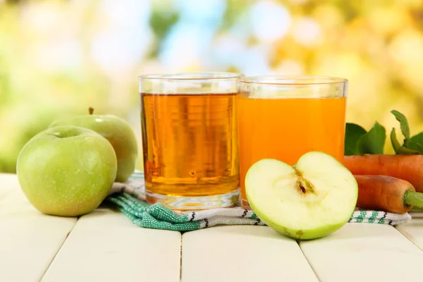Sklenice džusu, jablka a mrkev na bílý dřevěný stůl, na zeleném pozadí — Stock fotografie