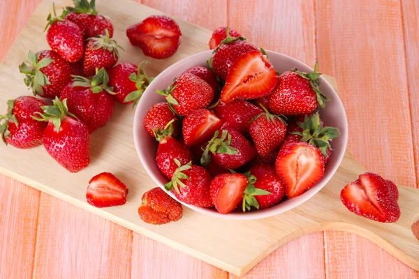 Strawberries in bowl on cutting board on wooden table — Stock Photo, Image