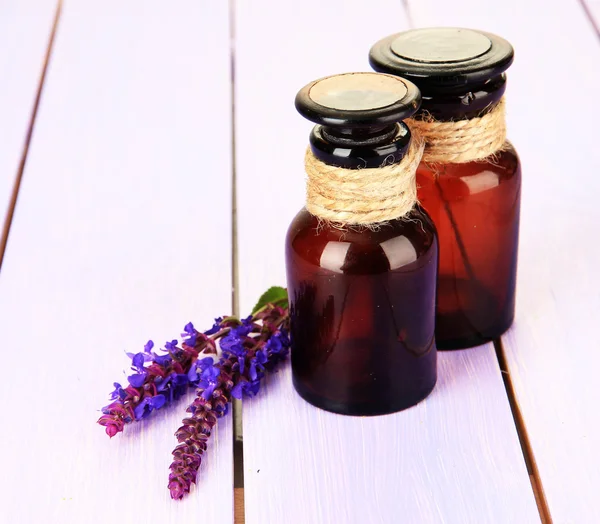 Geneeskundeflessen en salvia bloemen op paarse houten achtergrond — Stockfoto