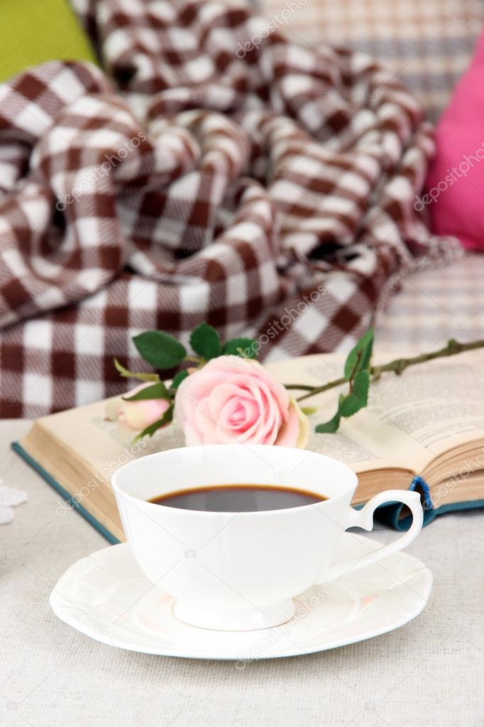 Composition with cup of drink, book and flowers on home interior background