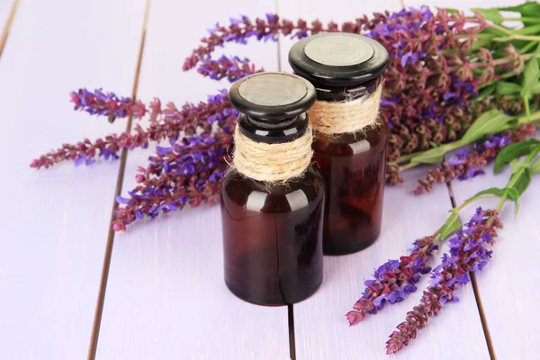 Medicine bottles and salvia flowers on purple wooden background — Stock Photo, Image