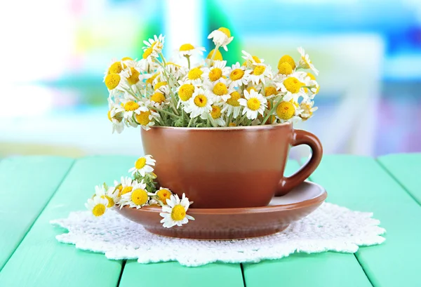 Bouquet of chamomile flowers in cup, on bright background — Stock Photo, Image