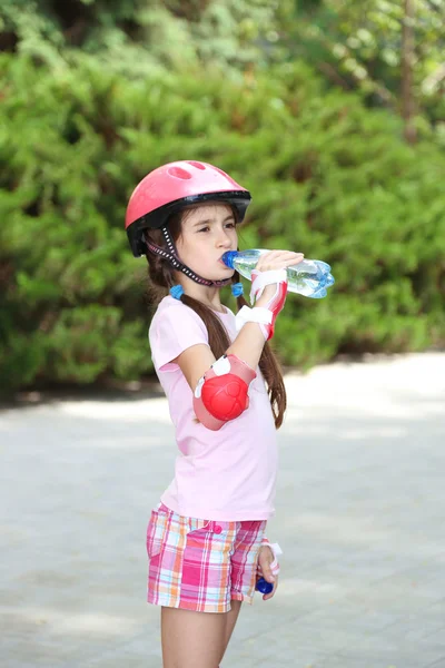 Little girl in roller skates drinking water at park — Stock Photo, Image