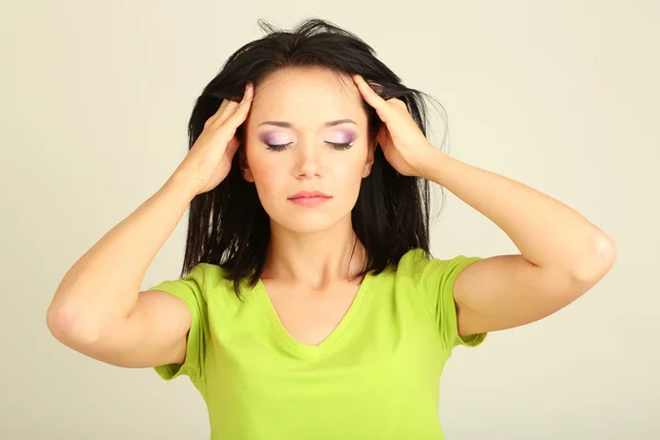 Mladá žena má bolesti hlavy na šedém pozadí — Stock fotografie