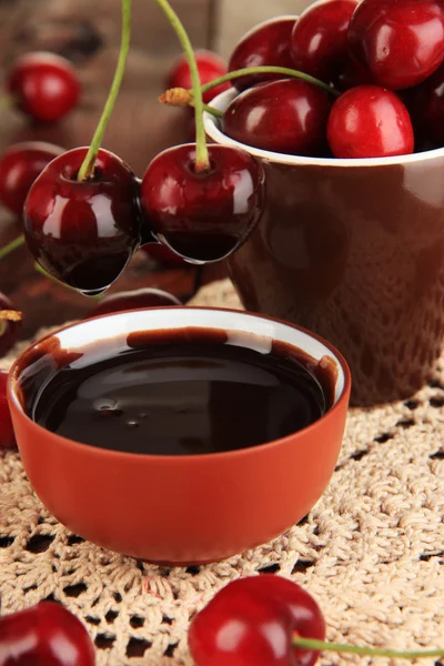 Bayas rojas maduras de cereza en taza y salsa de chocolate en primer plano de mesa de madera — Foto de Stock