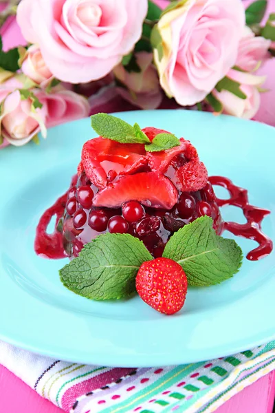 Finom zselés desszert a friss bogyós gyümölcsök, rózsaszín rózsa háttér — Stock Fotó