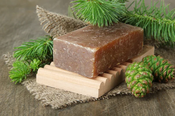 Ručně vyráběné mýdlo a zelené šišky na dřevěné pozadí — Stock fotografie