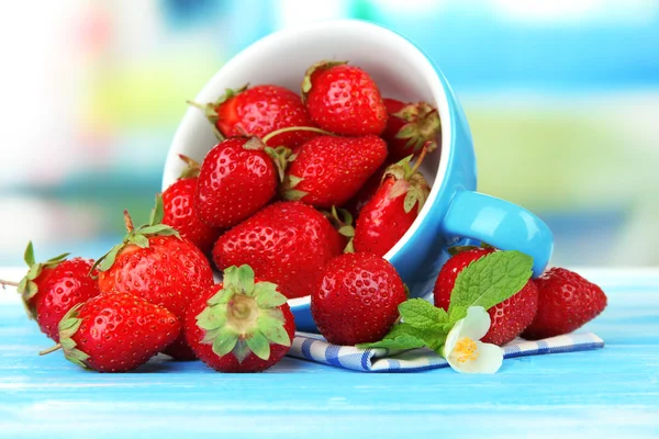 成熟的甜草莓在蓝色的木桌上的杯子 — 图库照片