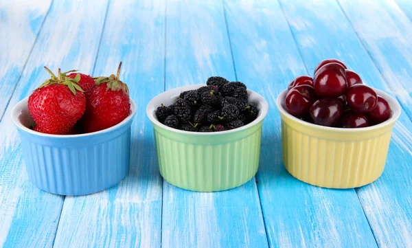 Ripe mulberries with cherry and strawberries in bowls on wooden background — Stock Photo, Image