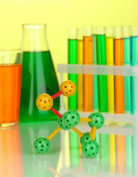 Molecule model and test tubes with colorful liquids on yellow background — Stock Photo, Image