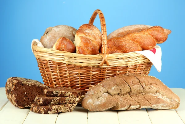 Composition with bread and rolls, in wicker basket on wooden table, on color background — Stock Photo, Image